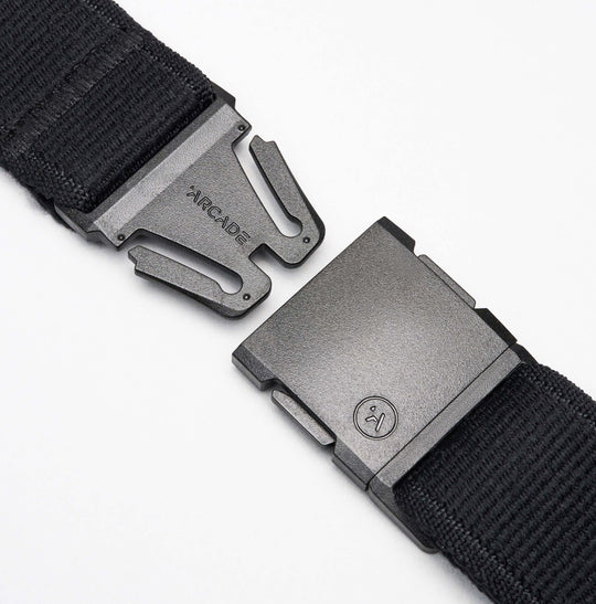 Close-up of the Arcade Belts Midnight Long Kit elastic stretch belt with a metal buckle, showing both separated ends. One end features the brand name Arcade, and the other has a small circular logo against a white background.