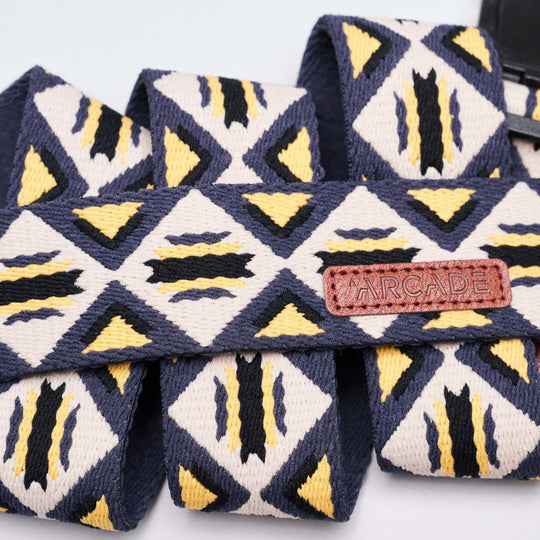 A close-up of the Vernan Kee fabric strap by Arcade Belts shows geometric shapes inspired by traditional rug patterns in navy blue, yellow, and white, with a brown leather tag featuring the brand's name.