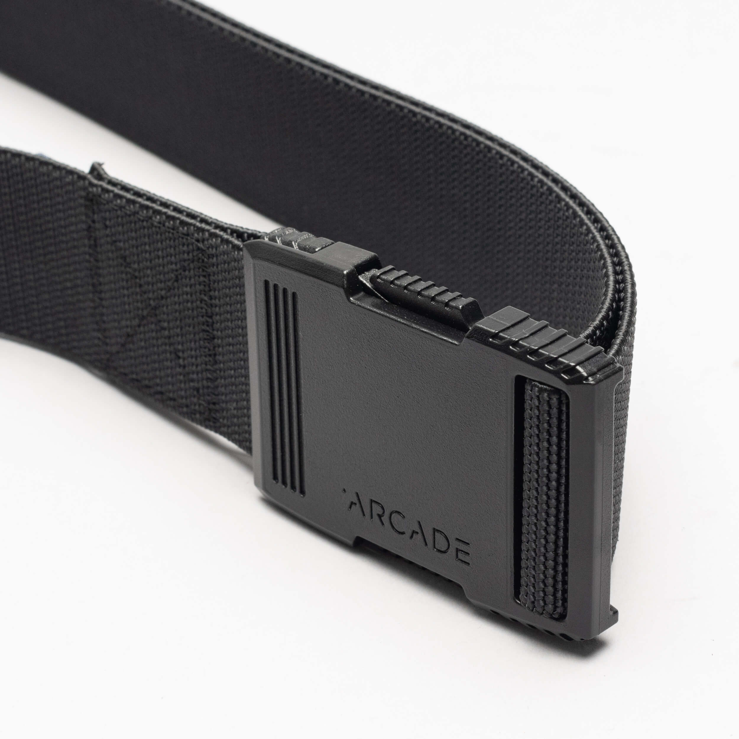A close-up of the Arcade Belts Hardware: a black elastic stretch belt with a rectangular black plastic buckle engraved with "ARCADE," shown against a white background.