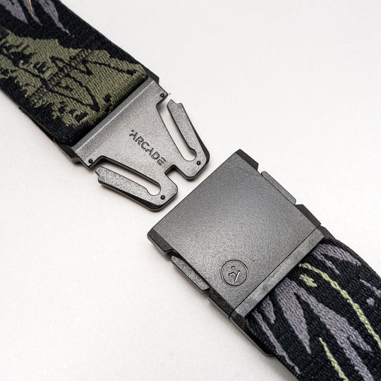 A close-up of the Arcade Belts Out of Range, featuring a metal buckle with visible branding, partially unclasped to reveal patterned green and black fabric.