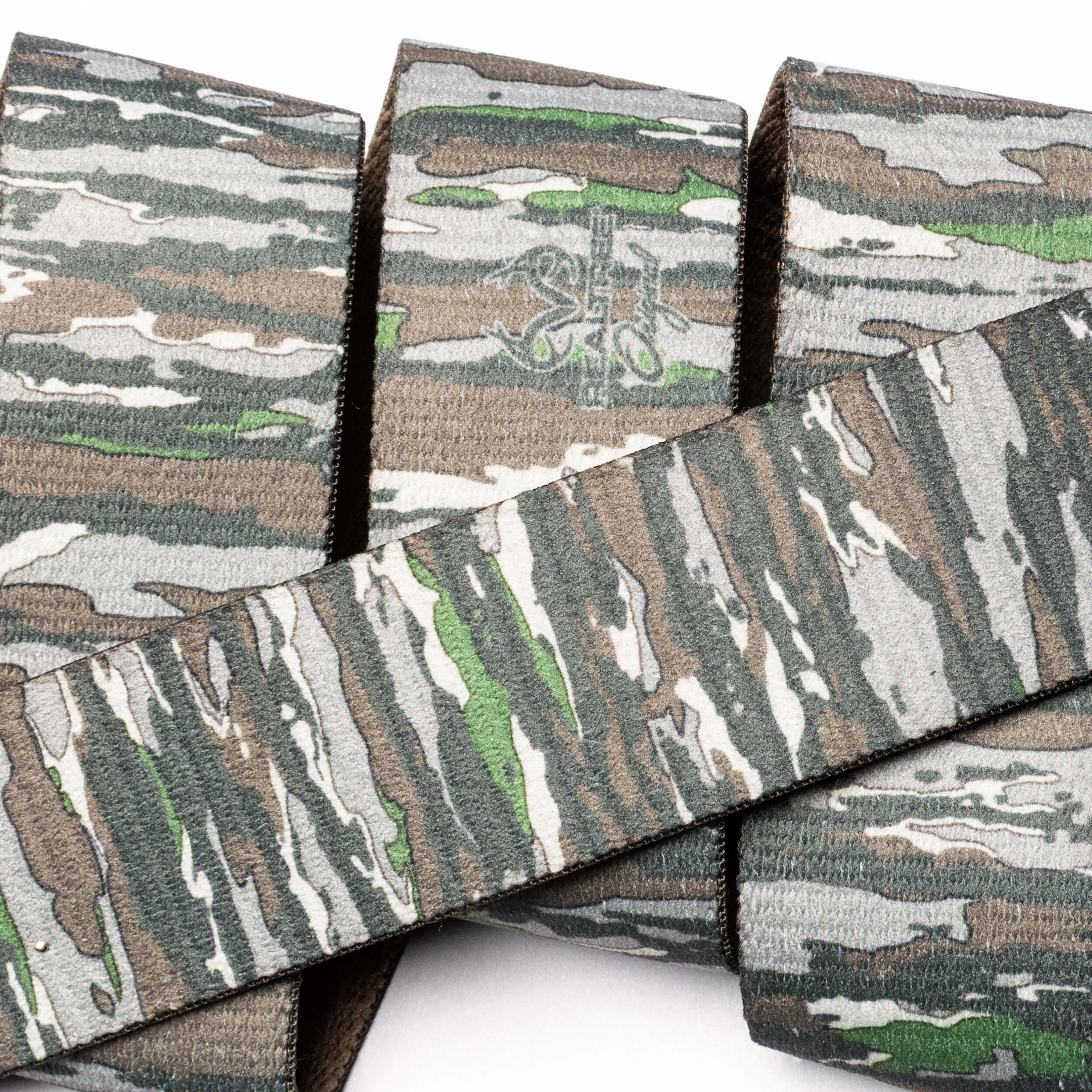 A close-up of Arcade Belts' Realtree Camo Original, featuring stretch webbing with fabric straps in green, brown, tan, and gray camouflage overlapping against a white background.